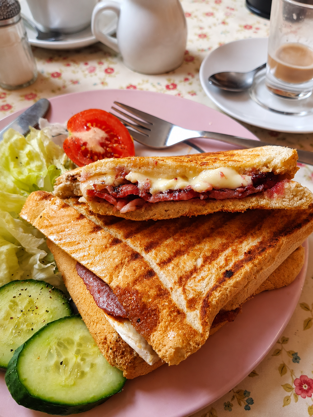 A toasted bacon and cheese sandwich served with cucumber and salad